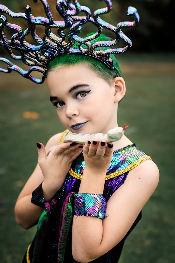 Child in a vibrant Medusa costume holding a snake toy outdoors.