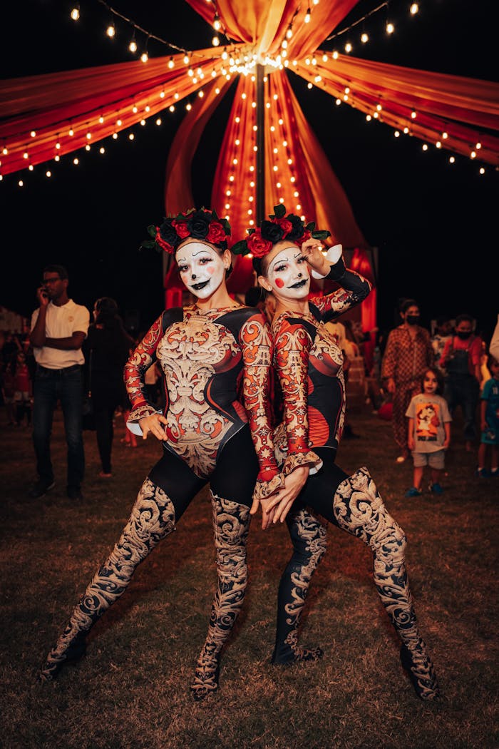 Two women in elaborate costumes and face paint pose at a vibrant night circus event.